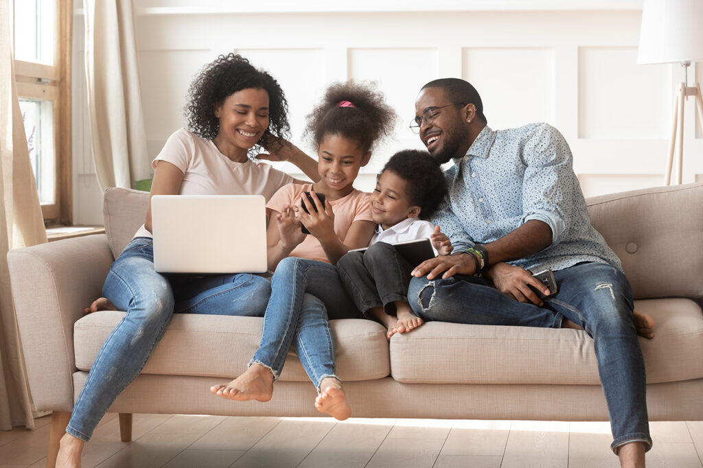 Family laughing and looking at a laptop on a couch together.